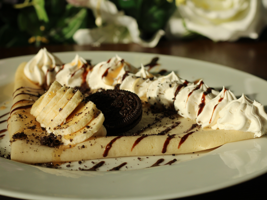A decadent crepe filled with crushed Oreo cookies and sliced bananas, topped with whipped cream and a drizzle of chocolate sauce and caramel sauce.