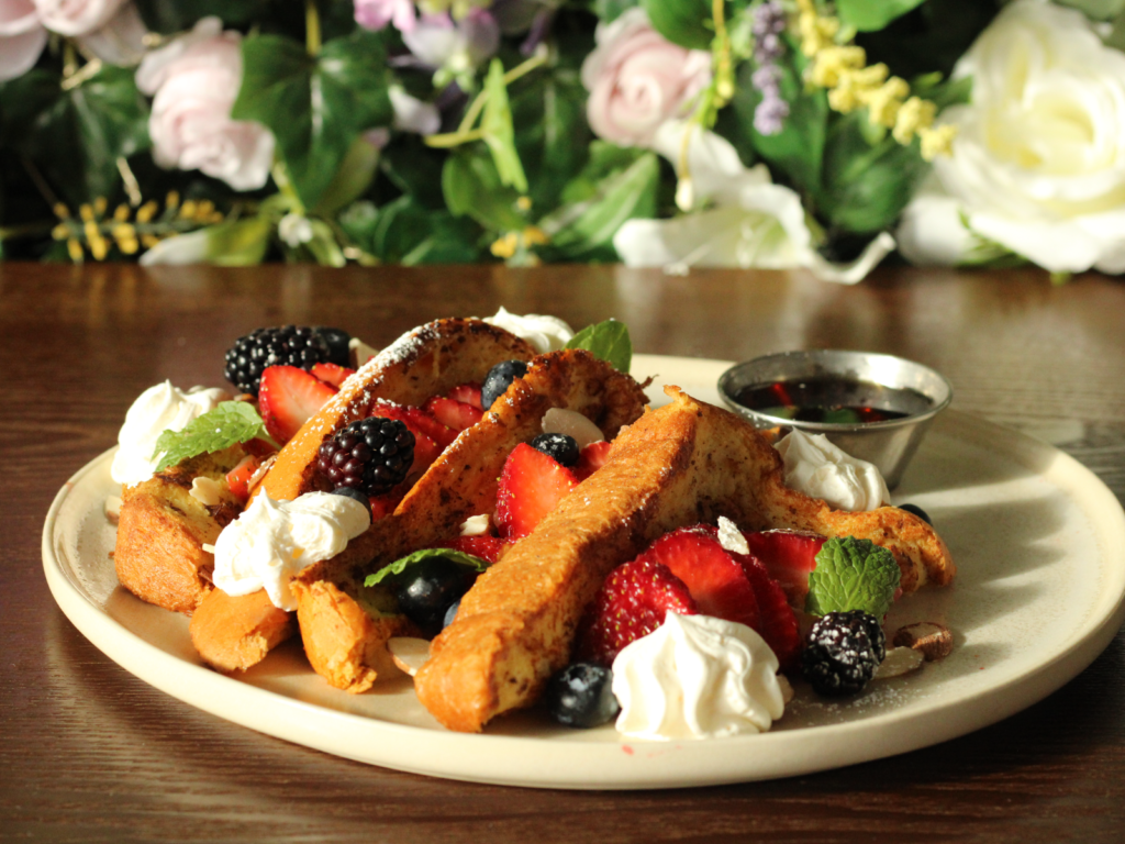 A golden, caramelized French toast crepe, dusted with powdered sugar and drizzled with maple syrup, served with a side of fresh fruit.