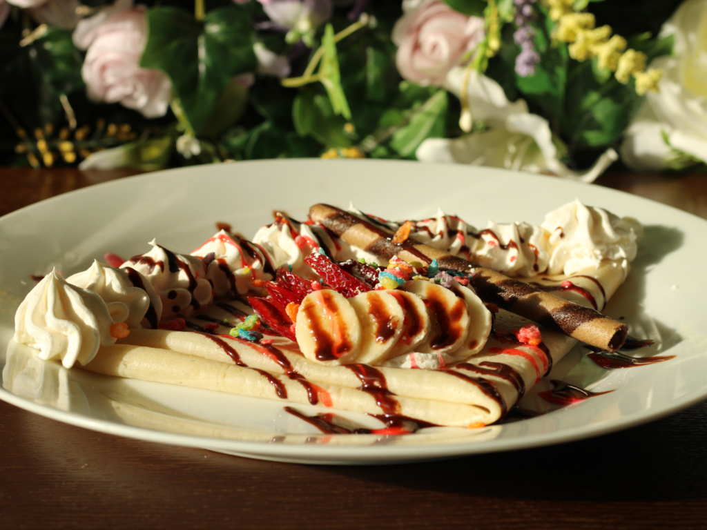 A freshly made crepe filled with sliced strawberries and bananas, topped with whipped cream and a drizzle of sweet sauce.