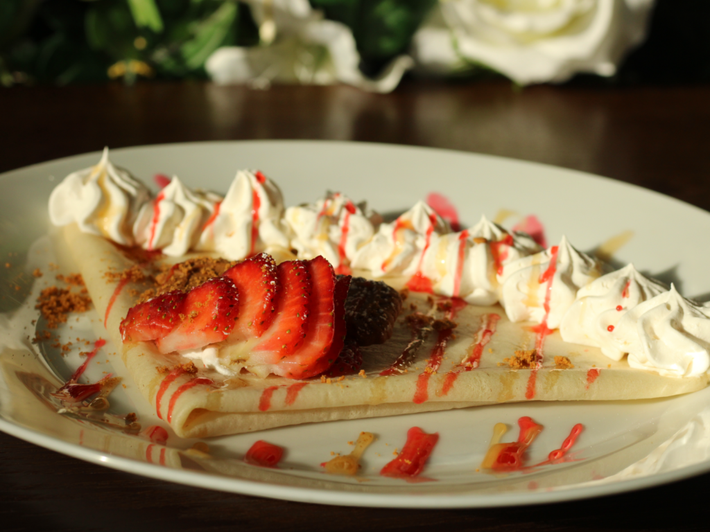 A delicate crepe filled with creamy Biscoff spread, tangy rosehip jam, and fresh sliced strawberries, folded and topped with a touch of sweetness.